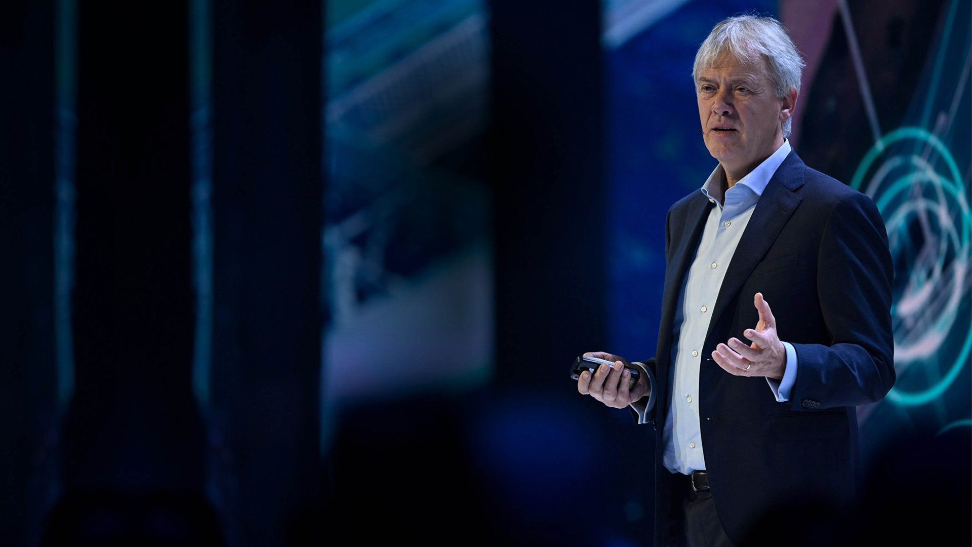 A picture of Peter Wennink giving a speech on stage, holding a remote control in one hand.