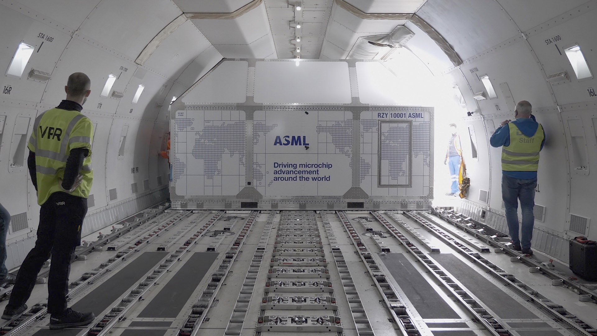 Three people unloading a lithography machine from an airplane